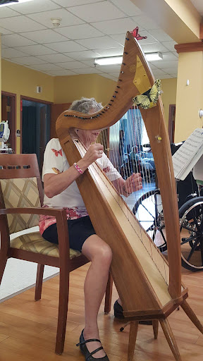 An elderly individual joyfully playing the harp in a welcoming indoor setting.