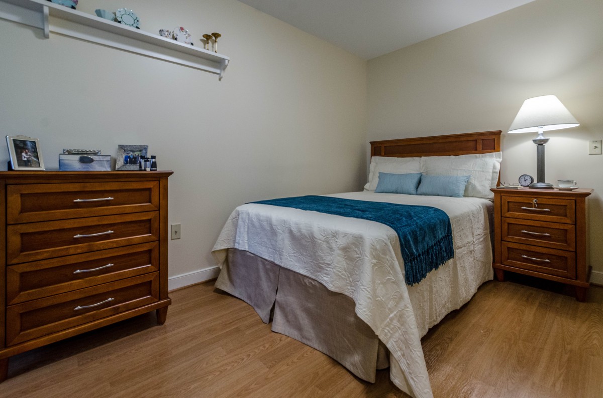A neatly arranged bedroom with a bed, dresser, and wooden flooring.