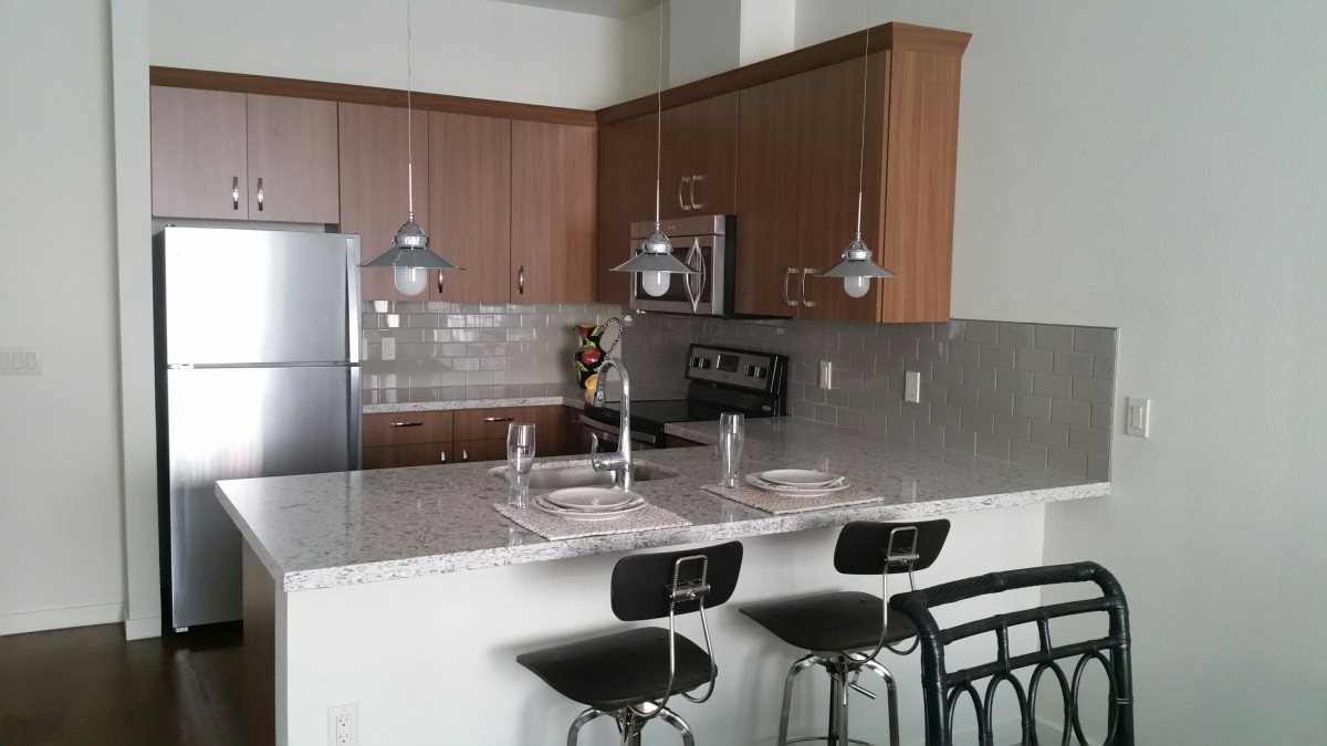 A modern kitchen with a sleek countertop, bar stools, and pendant lighting.