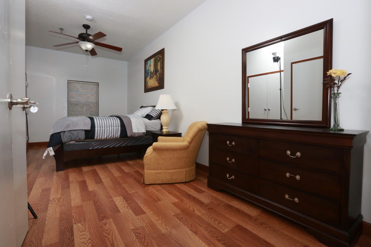 A neatly arranged bedroom featuring a bed, dresser with mirror, and chair on hardwood flooring.