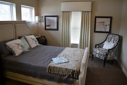 A cozy, well-decorated bedroom featuring a neatly made bed, framed artwork, and elegant curtains.