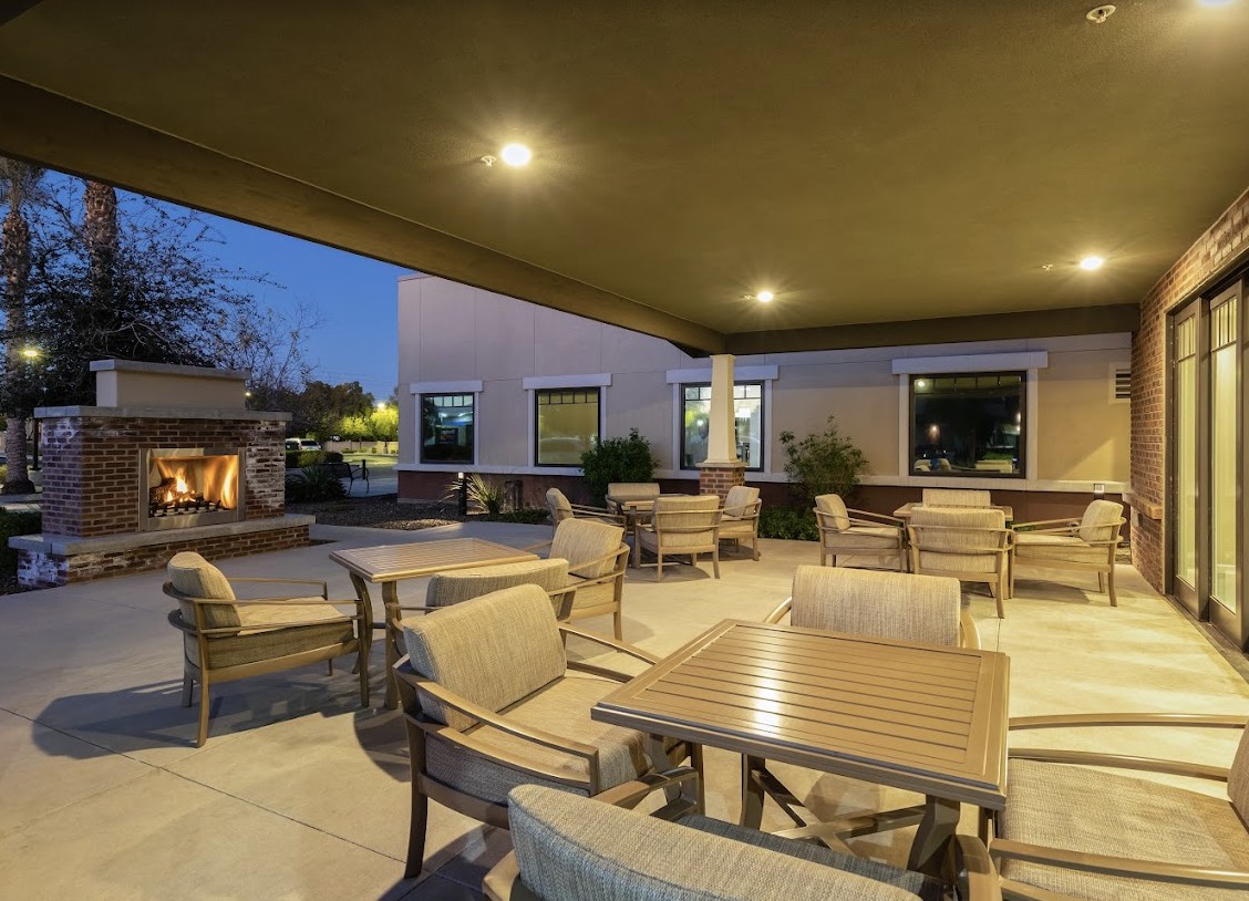 Cozy outdoor patio with seating and a fireplace, illuminated in the evening.