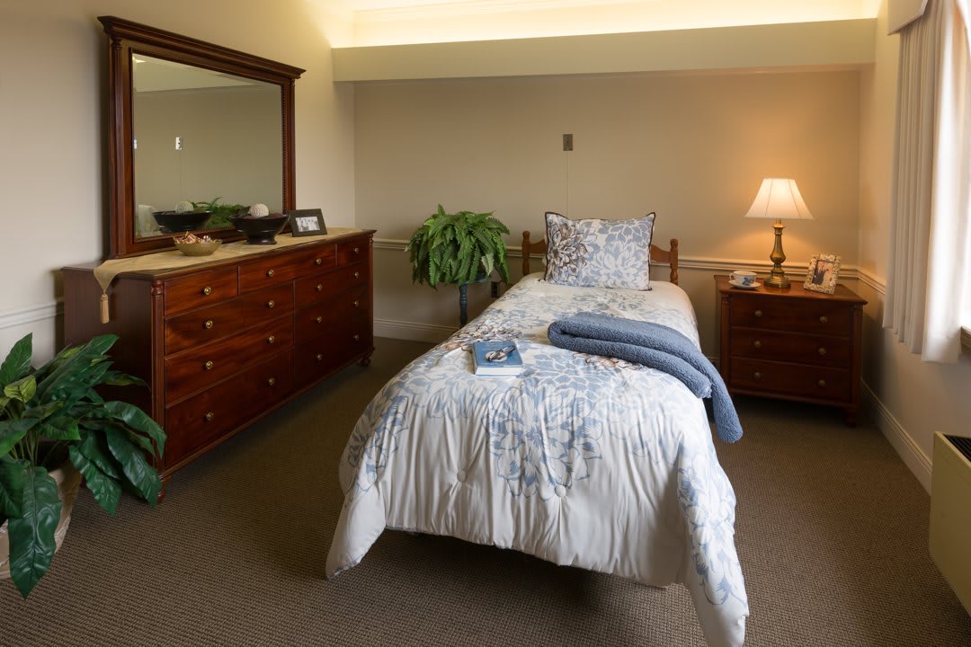 A cozy bedroom with a single bed, dresser, and lamp.