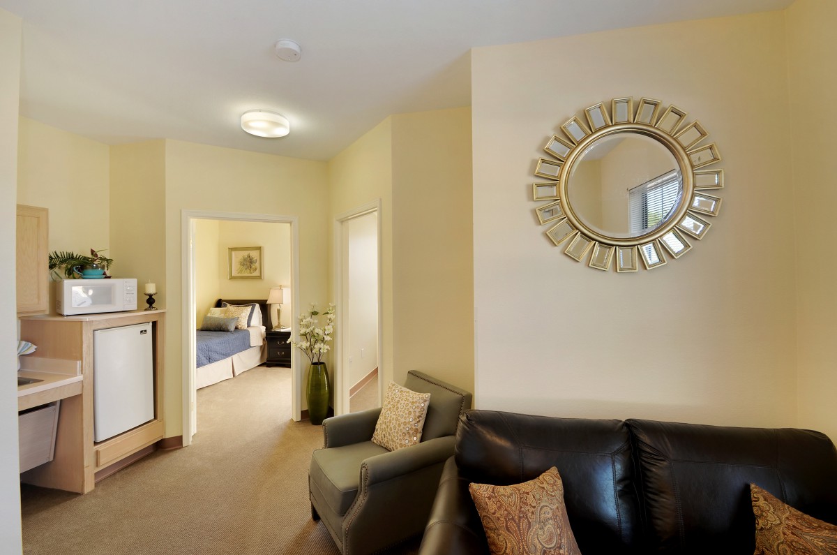 A cozy living room with a round decorative mirror and a view into the bedroom.