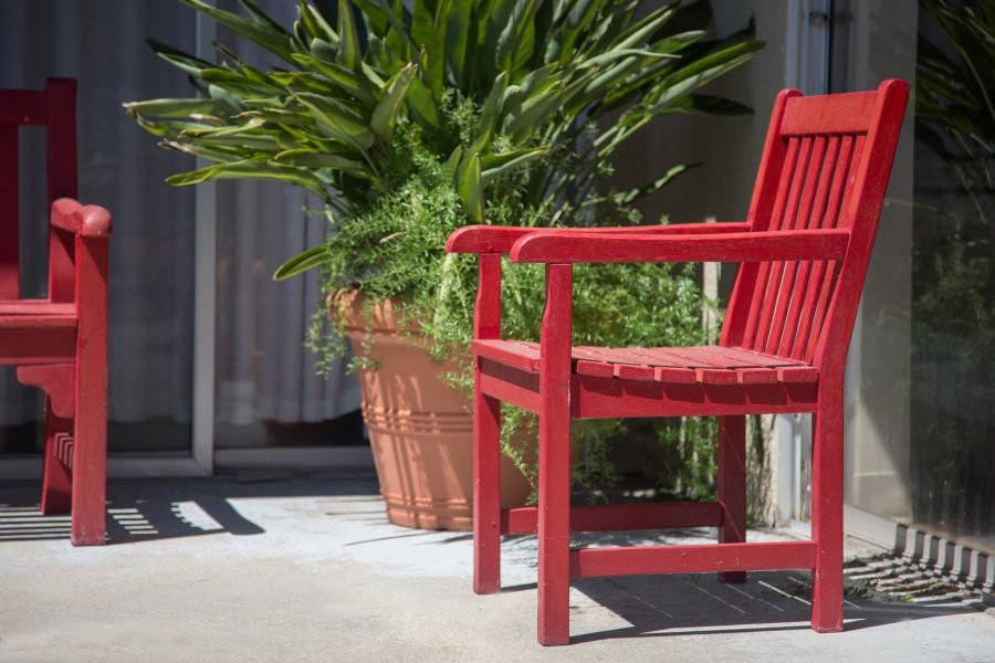 A bright red chair on a sunlit patio next to a large potted plant.
