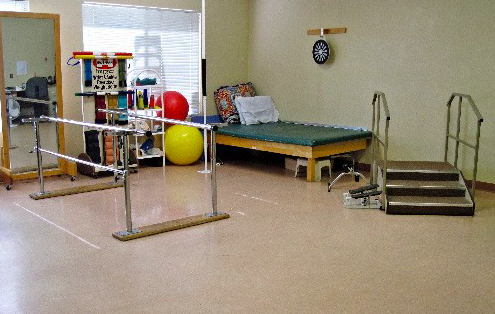 A well-equipped physical therapy room featuring exercise balls, a bed, and parallel bars for rehabilitation.