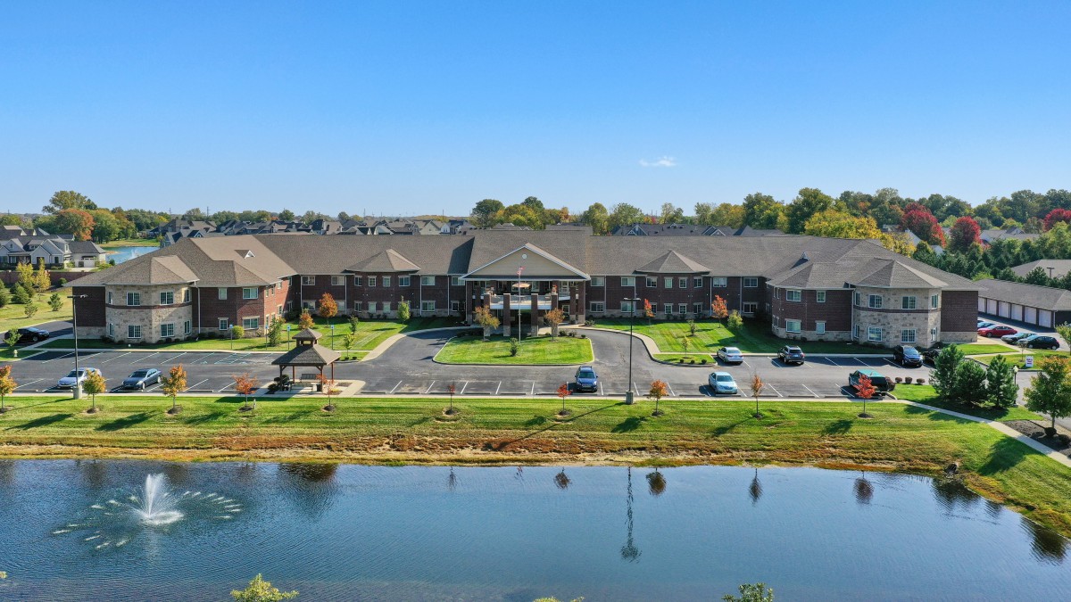 A large residential apartment complex near a tranquil lake with cars parked in front.