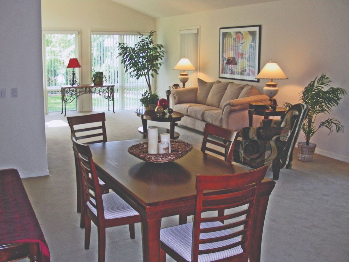 A cozy living room with a dining area featuring a wooden table, chairs, and a comfortable sofa.