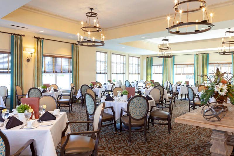 An elegant dining room with neatly arranged tables and chairs, featuring large windows and decorative chandeliers.