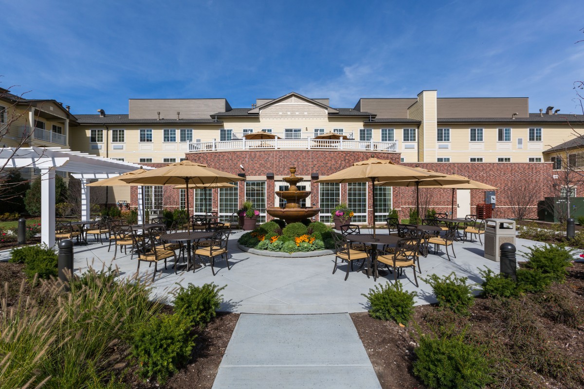 Outdoor seating area with tables, chairs, and a fountain in front of a residential building.