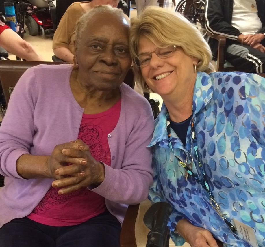 Two women smiling and sitting closely together indoors, showing a sense of friendship and warmth.