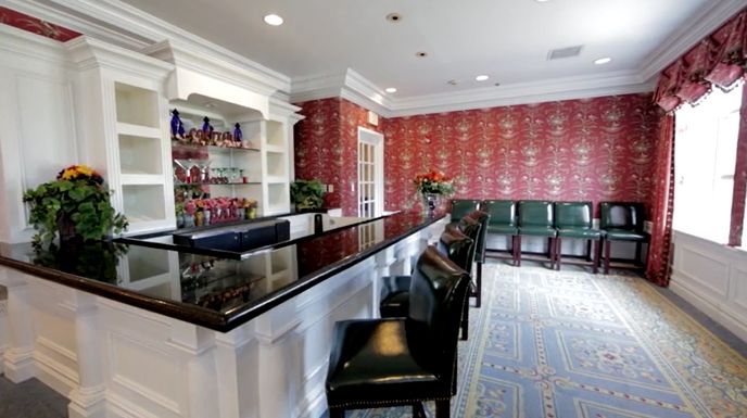 A stylish bar with comfortable seating and a well-stocked counter, featuring red wallpaper and elegant furnishings.