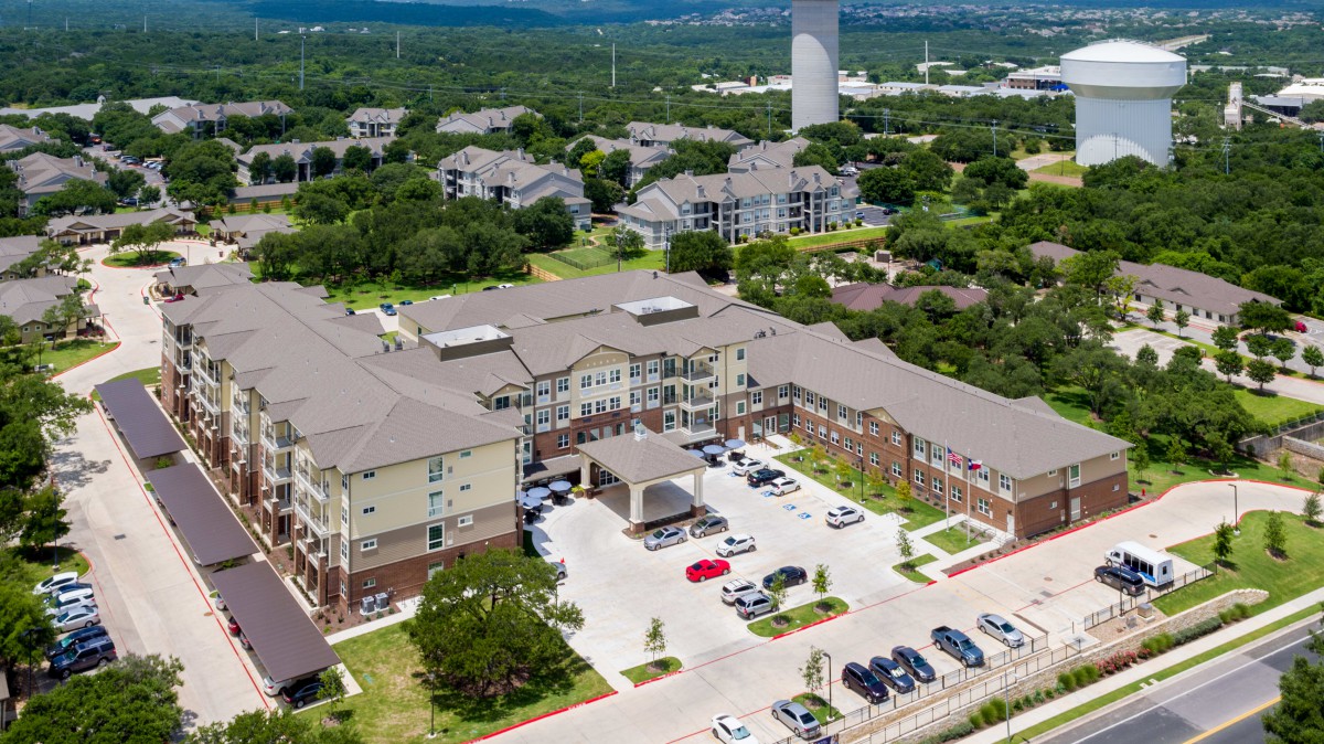 Aerial view of a large residential building surrounded by a parking lot and greenery.