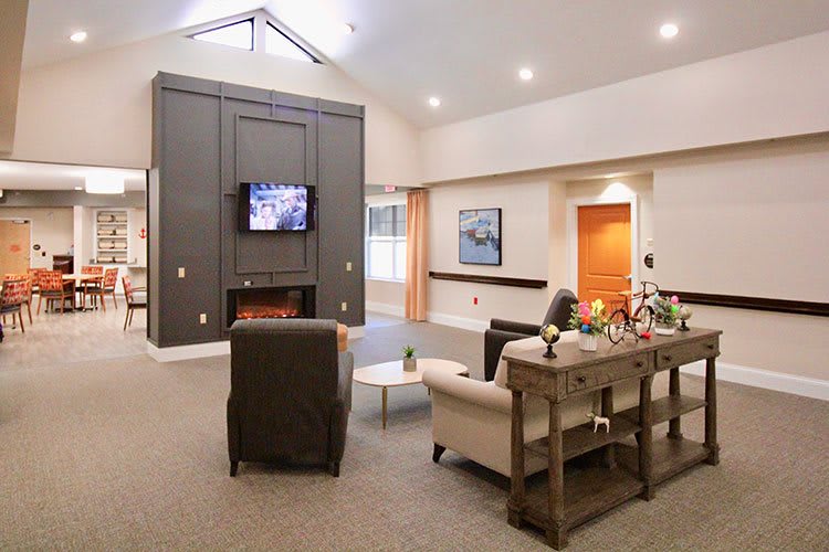 A cozy living room with modern furnishings, including a sofa and chairs facing a television above a fireplace.