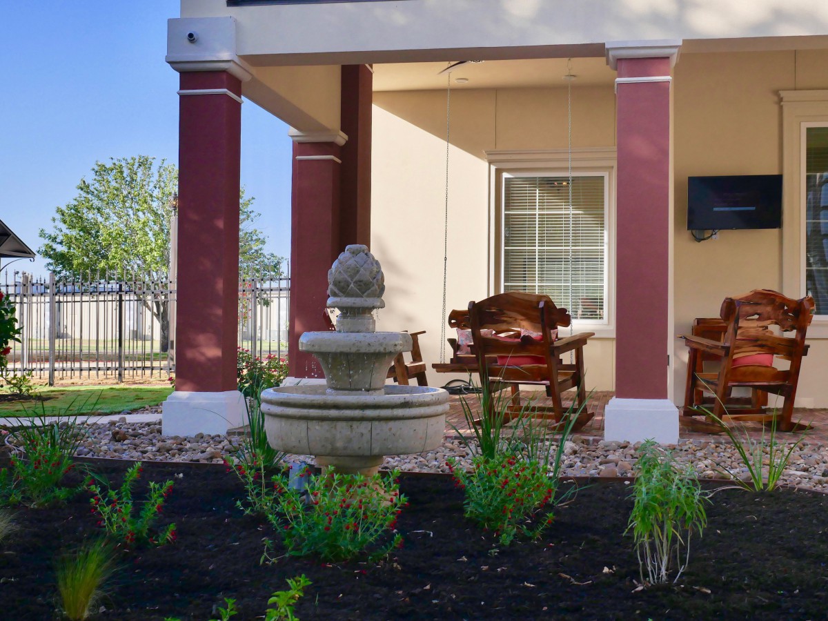 A serene patio with a fountain, surrounded by landscaped greenery and comfortable outdoor seating.