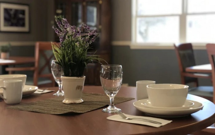A neatly set dining table with a plant centerpiece, glassware, and a bowl.