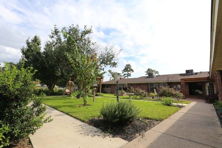 A scenic view of a garden with a pathway, surrounded by lush greenery and trees, adjacent to a building.