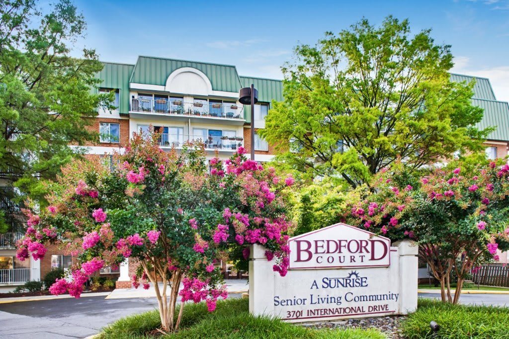 The image shows a senior living community named Bedford Court, surrounded by trees and flowers.
