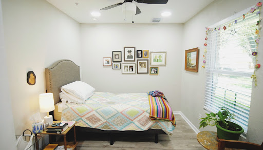 A cozy and well-decorated bedroom featuring a neatly made bed with colorful bedding and an array of framed pictures on the wall.
