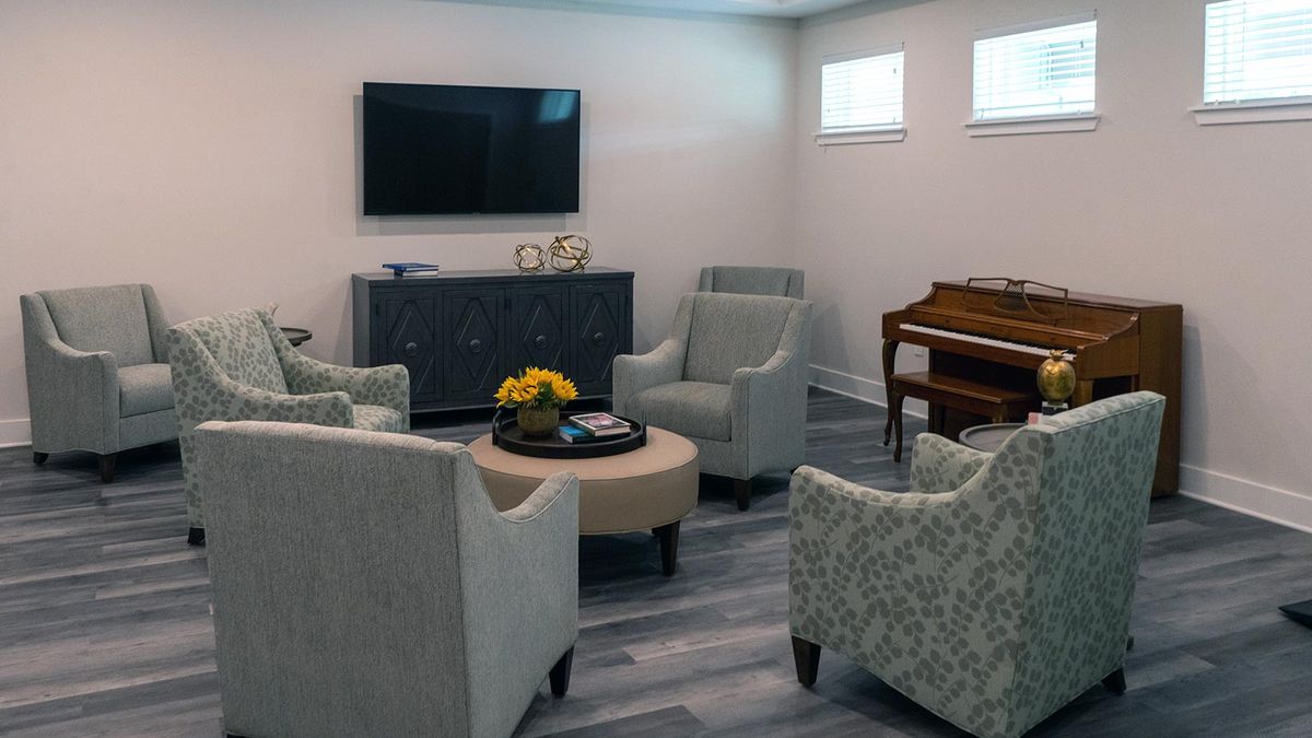 A cozy living room with elegant furniture, including a television, chairs, a piano, and a round table with decor.