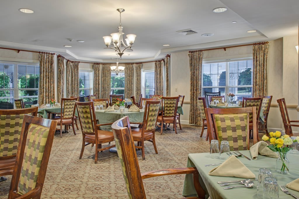 A well-decorated dining area with elegant tables and chairs arranged under chandeliers, featuring large windows with curtains.