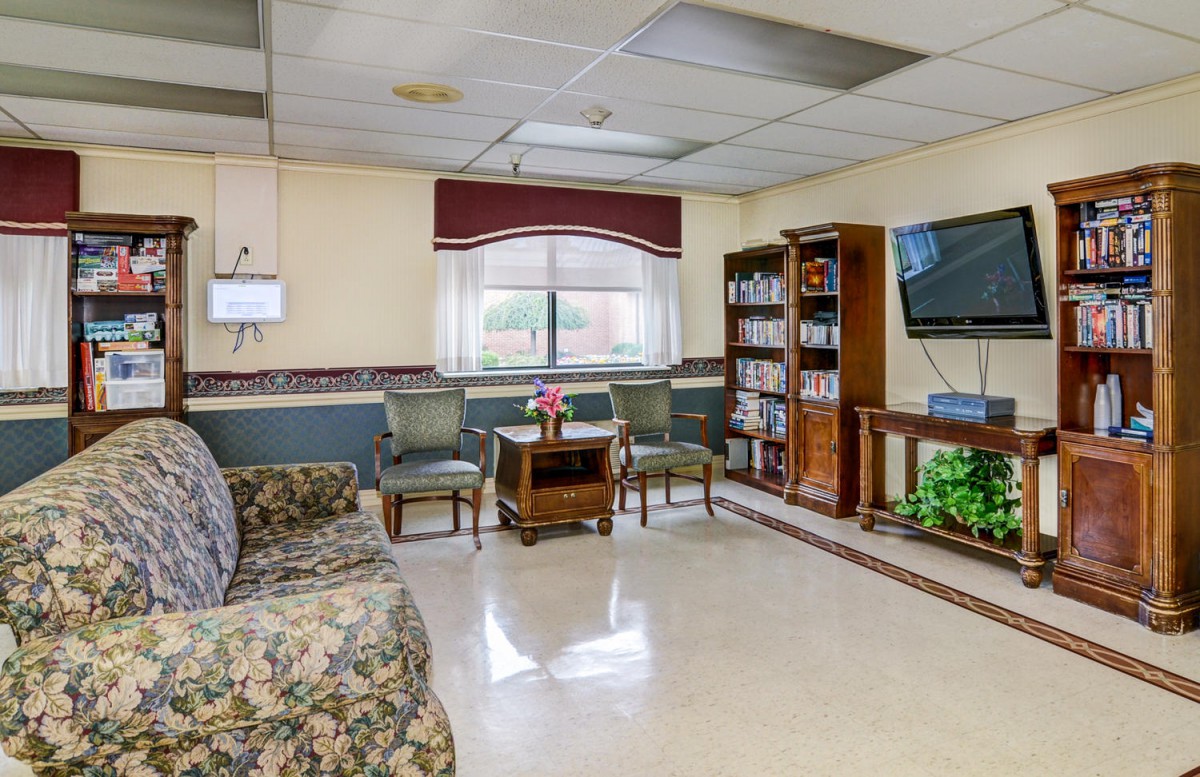 A cozy waiting room with comfortable seating, a large television, and bookshelves filled with reading materials.