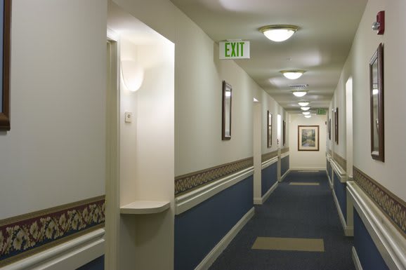 A well-lit hallway with a blue and white color scheme, featuring an exit sign and framed pictures.