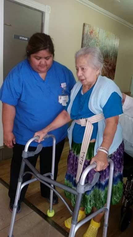 A caregiver assisting an elderly woman with a walker.