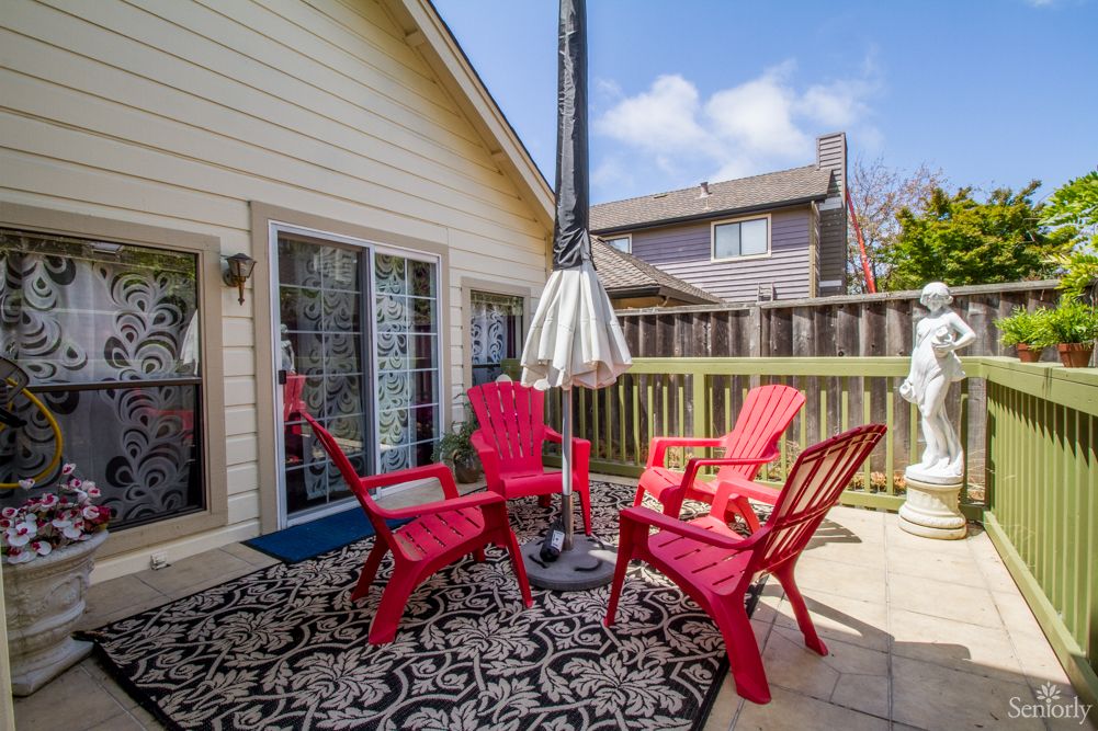 A cozy outdoor patio area featuring red chairs, a central umbrella, and a decorative rug on a wooden deck.
