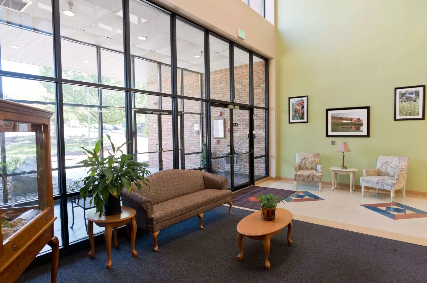 A spacious lobby with a sofa, small tables, plants, and large windows.