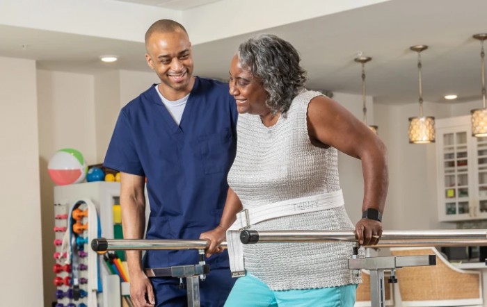 A healthcare professional assists an elderly woman during a physical therapy session.