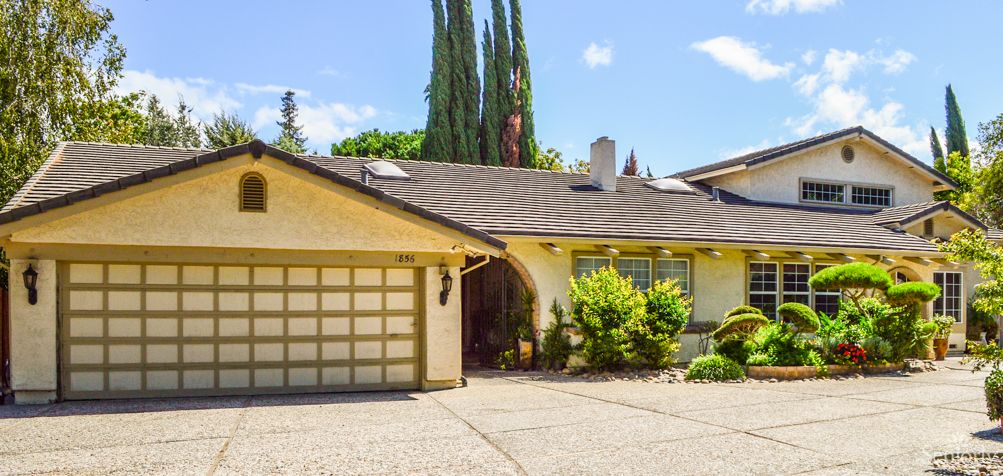 A suburban house with a garage and driveway, surrounded by trees under a clear sky.