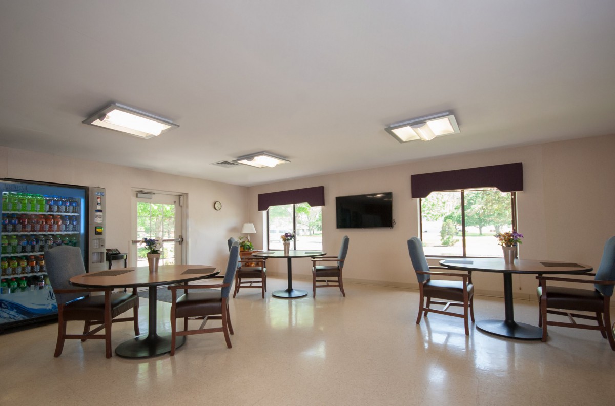 A clean and spacious dining area with tables, chairs, windows, and a wall-mounted television.