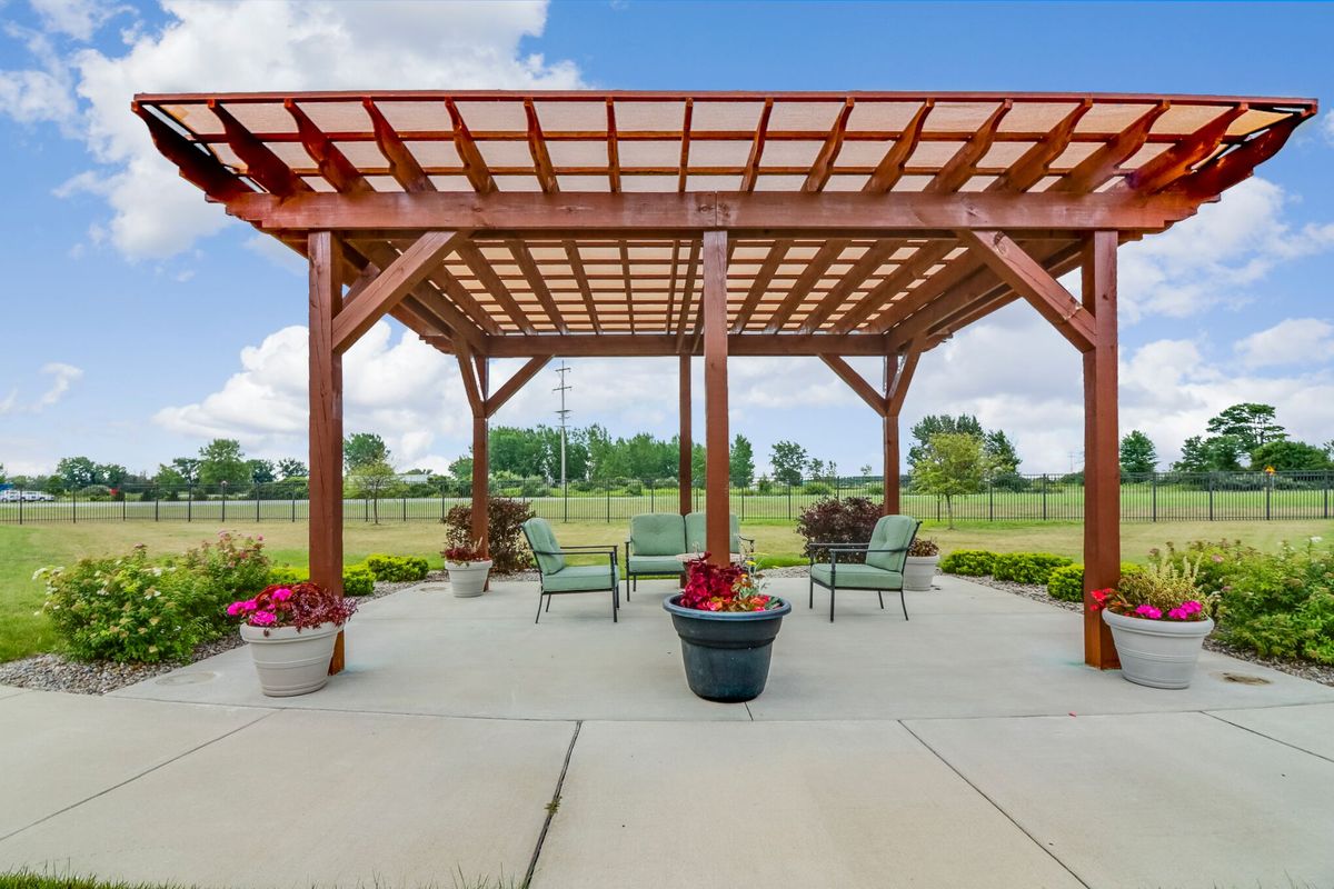 A spacious patio featuring a wooden pergola, surrounded by outdoor seating and vibrant potted plants, under a clear blue sky.