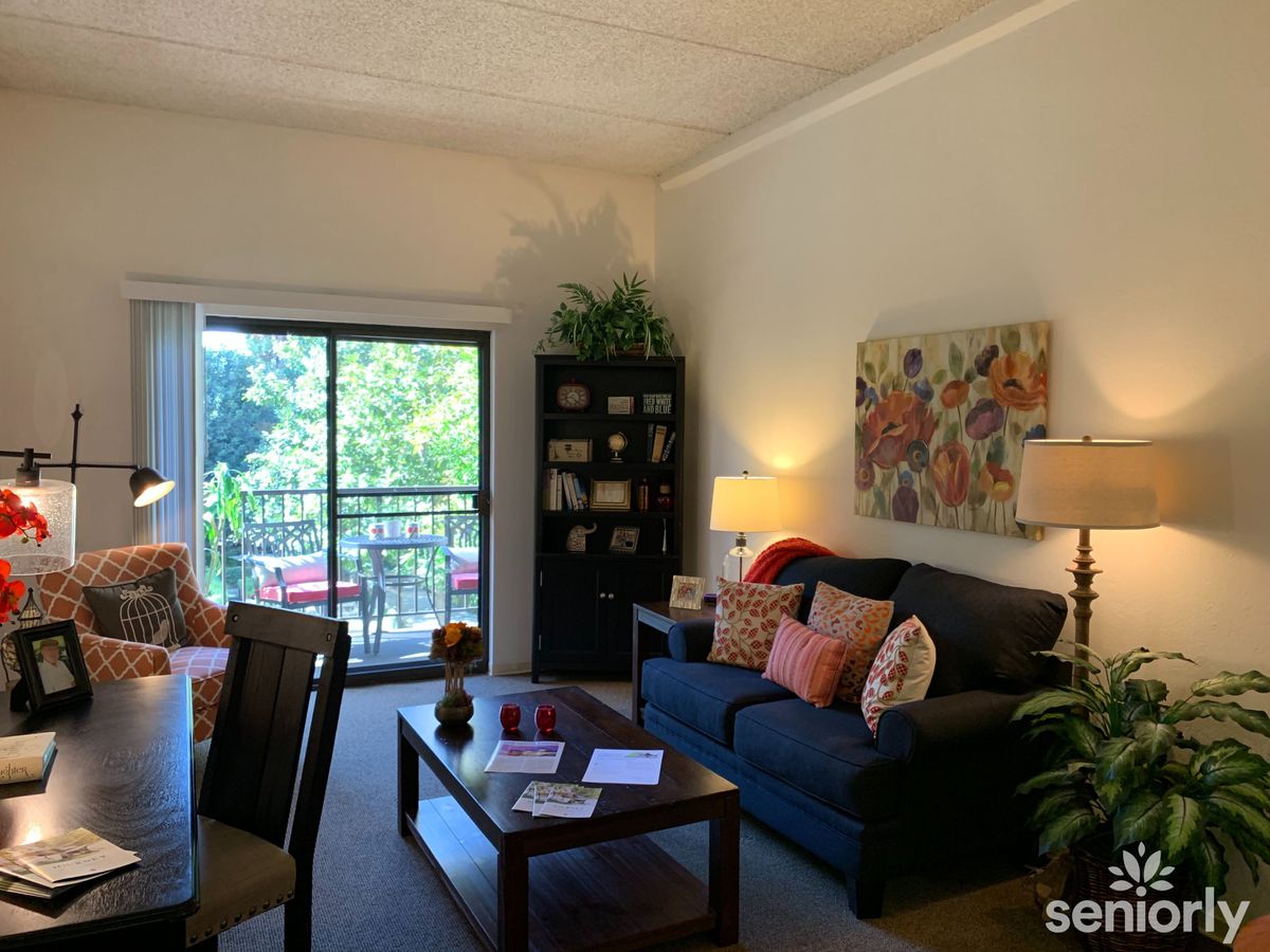A cozy living room with a sofa, coffee table, bookshelf, and large window allowing natural light.
