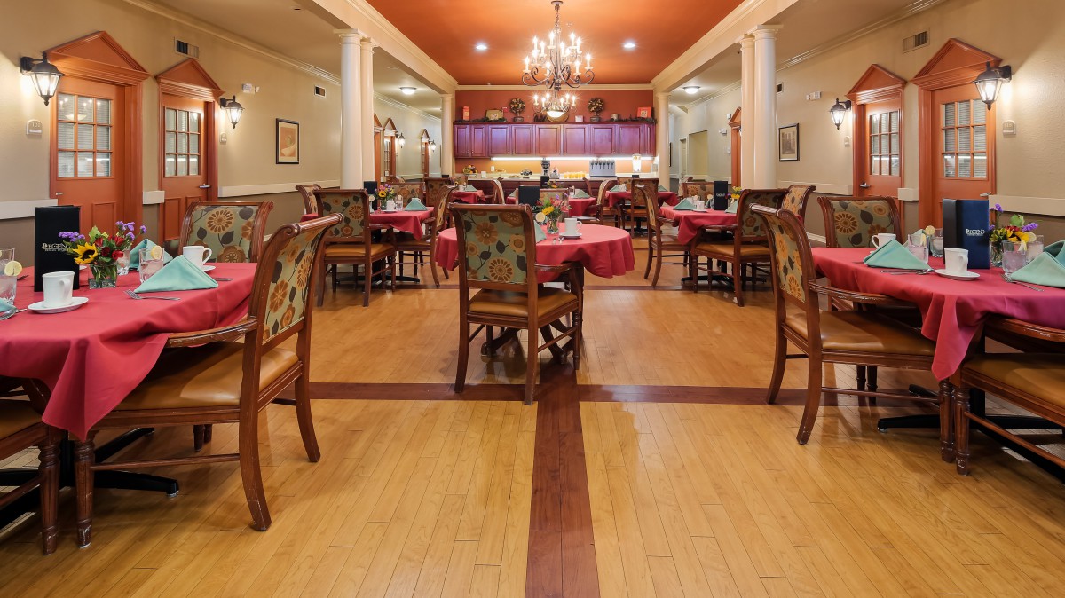 An elegant restaurant interior featuring dining tables set with red tablecloths, wooden chairs, and chandeliers.