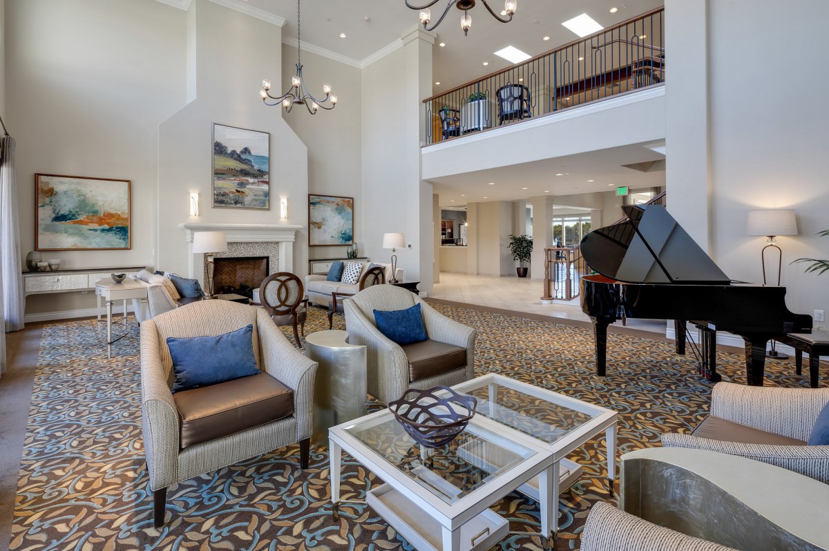 A spacious and elegantly decorated living room featuring comfortable seating, a grand piano, and tasteful artwork.