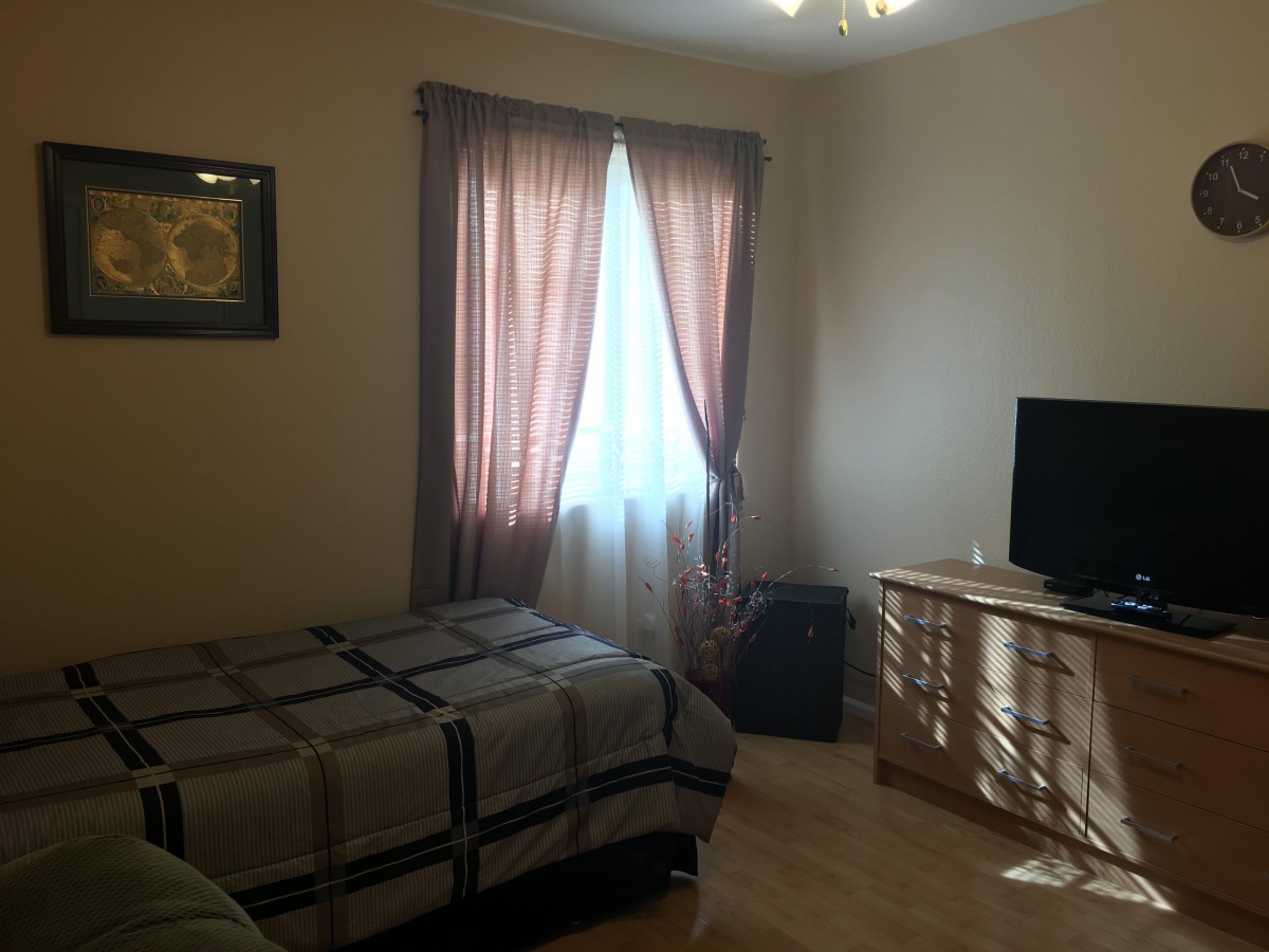 A cozy bedroom with a bed, TV, and dresser next to window curtains.