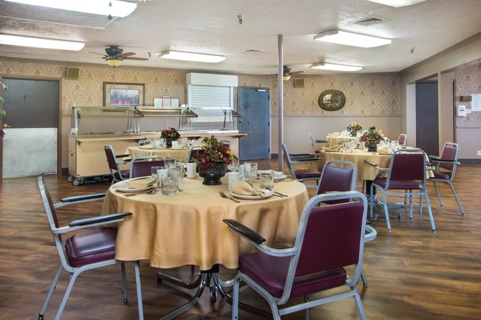 A dining room with round tables covered in yellow tablecloths and red chairs, set for a meal.