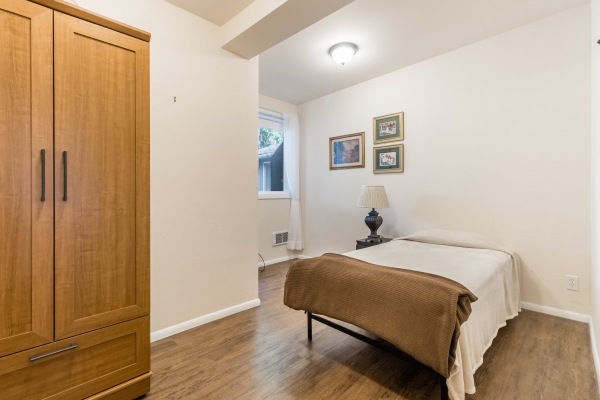 A cozy bedroom with a single bed, wardrobe, lamp, and framed artwork on the wall.
