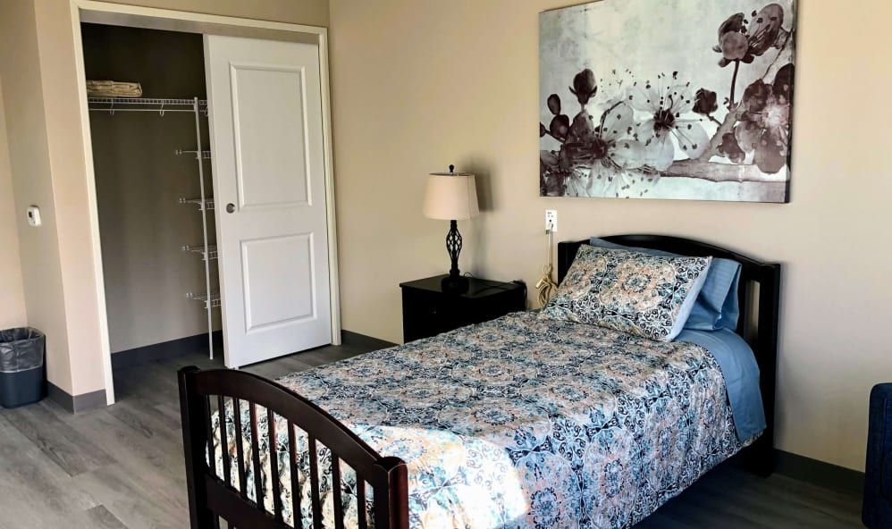 A cozy bedroom featuring a single bed with floral bedding, a bedside lamp, and wall art.