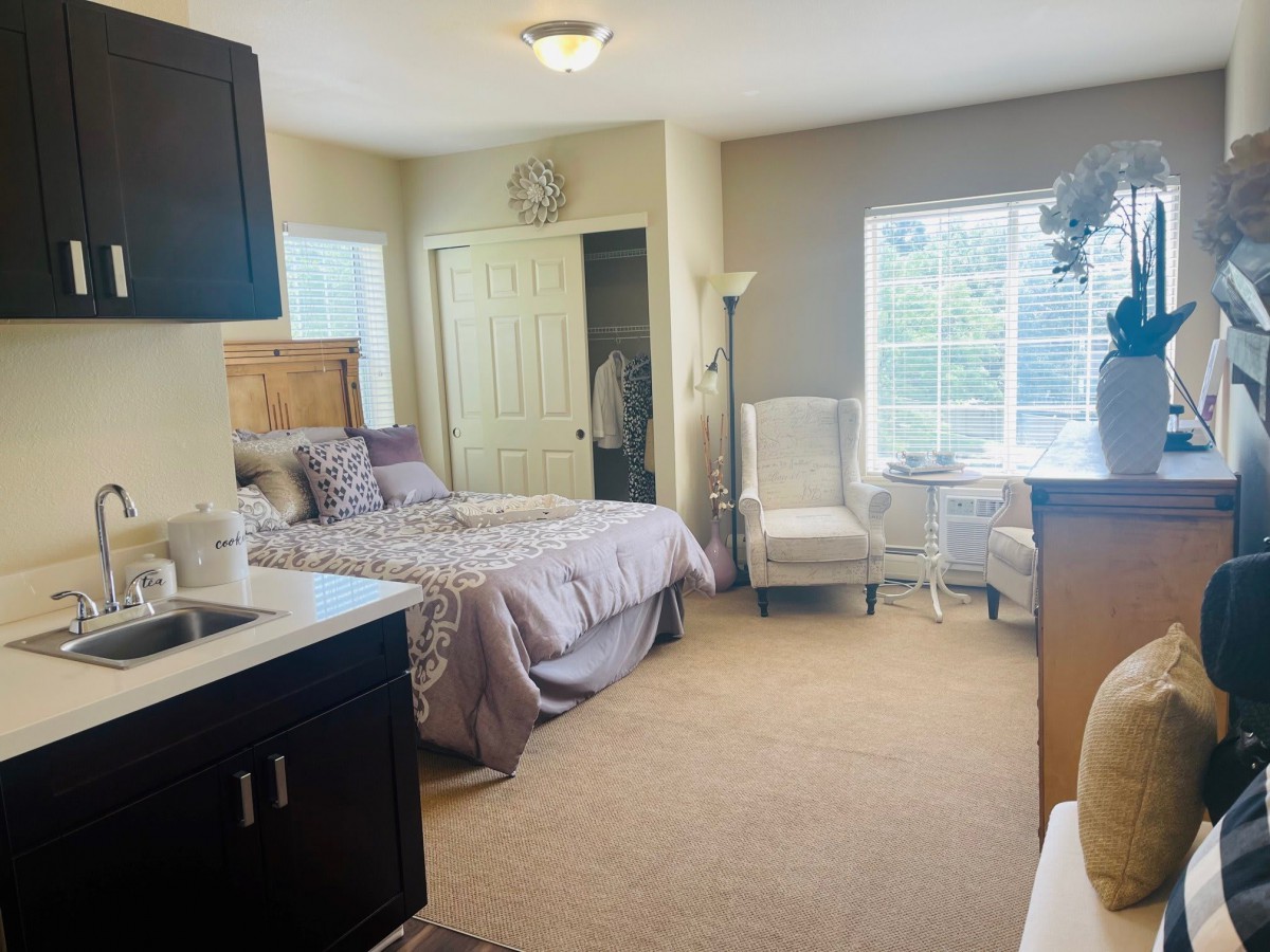 A cozy bedroom with a neatly made bed, comfortable chair by the window, and soft natural lighting.