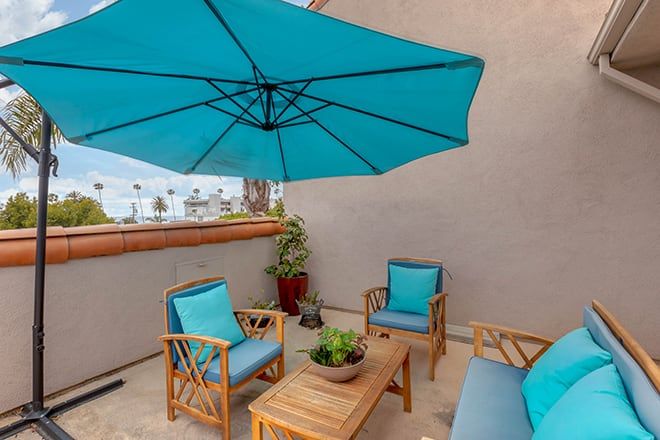 A cozy outdoor patio setup with wooden furniture and a large blue umbrella.
