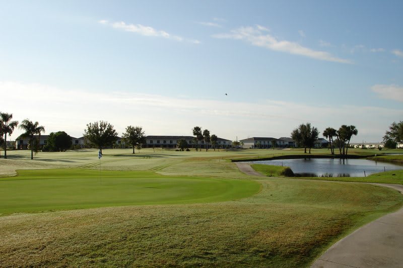 A scenic view of a golf course with lush green grass, trees, and a pond under a clear morning sky.