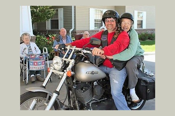 Two people, including an elderly person, enjoying a motorcycle ride together outdoors.