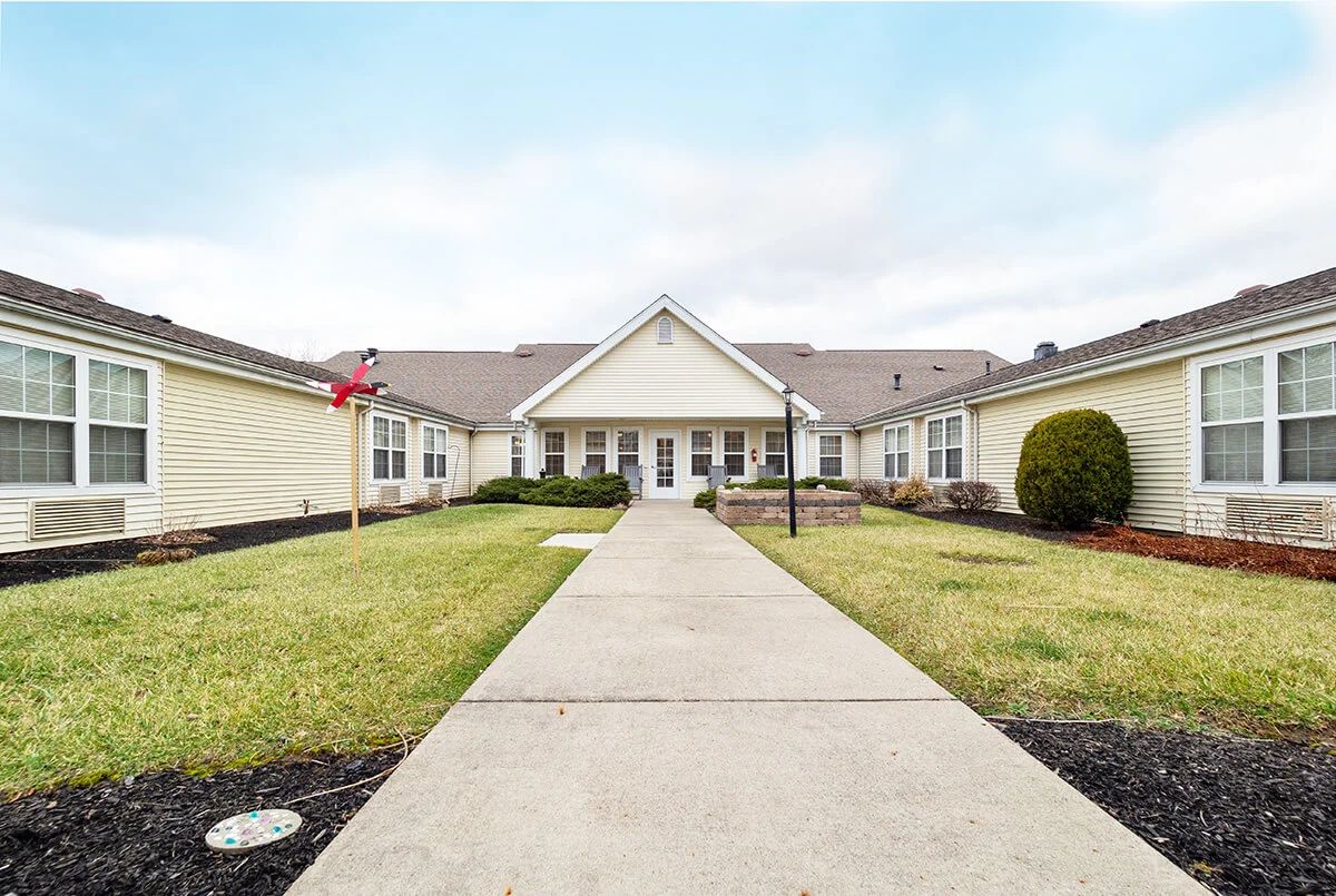 A wide pathway leads to a large residential building surrounded by a well-kept lawn.