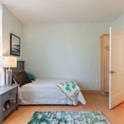 A minimalist bedroom with a neatly made bed, a nightstand with a lamp, and an open door.