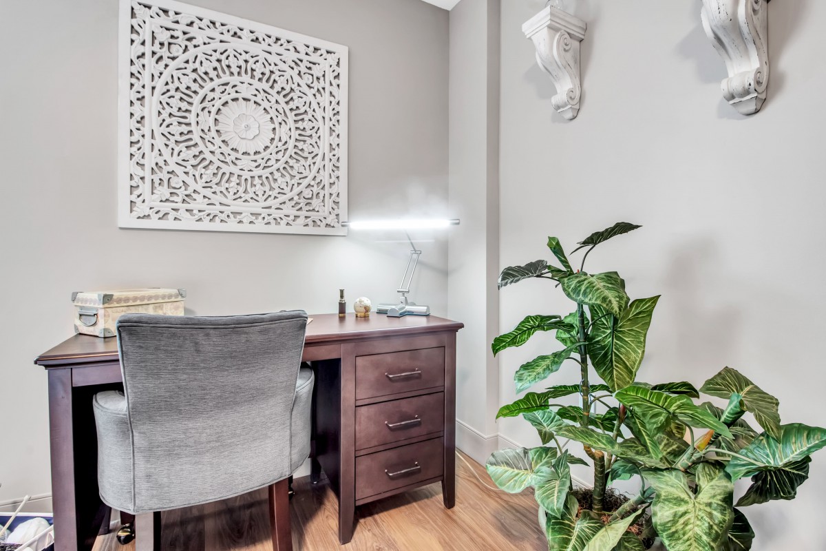 A cozy home office setup with a wooden desk, comfortable chair, decorative wall art, and an indoor plant.