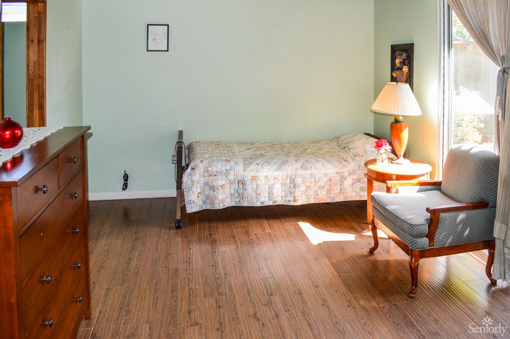 A simple bedroom with a single bed, a chair, and a lamp on a wooden floor.