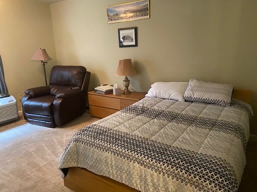 A cozy bedroom featuring a bed with a patterned quilt, an armchair, and two lamps on nightstands.